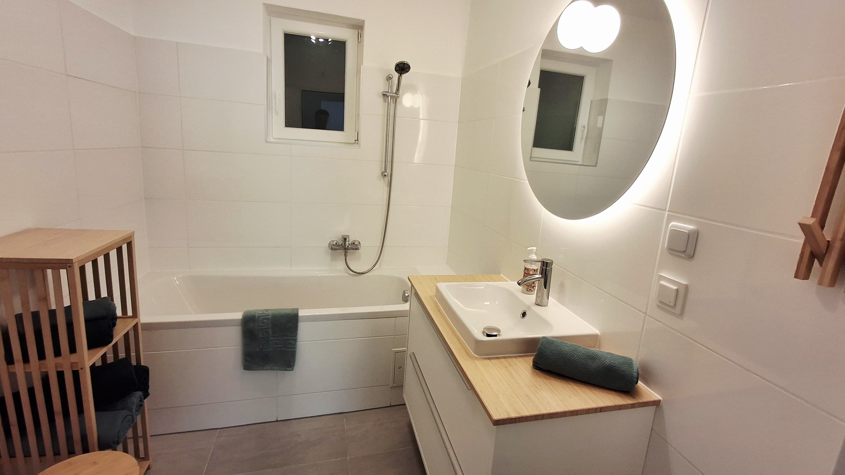 Modernes Badezimmer mit Badewanne, Waschbecken und beleuchtetem Spiegel.