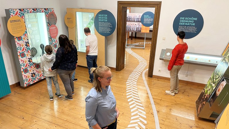 Menschen in einem Museum betrachten interaktive Ausstellungen mit Texttafeln und Exponaten.