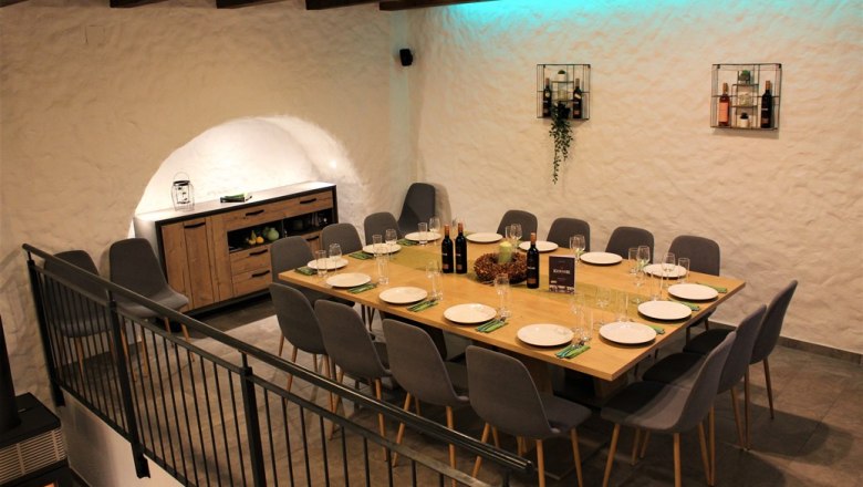 Ein stilvoll gedeckter Tisch in einem Weinkeller mit modernen grauen St&uuml;hlen und dekorativer Beleuchtung.