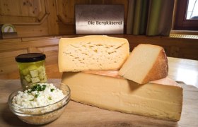 Verschiedene Käsesorten auf einem Holzbrett mit einem Glas eingelegtem Käse und einer Schüssel Frischkäse.