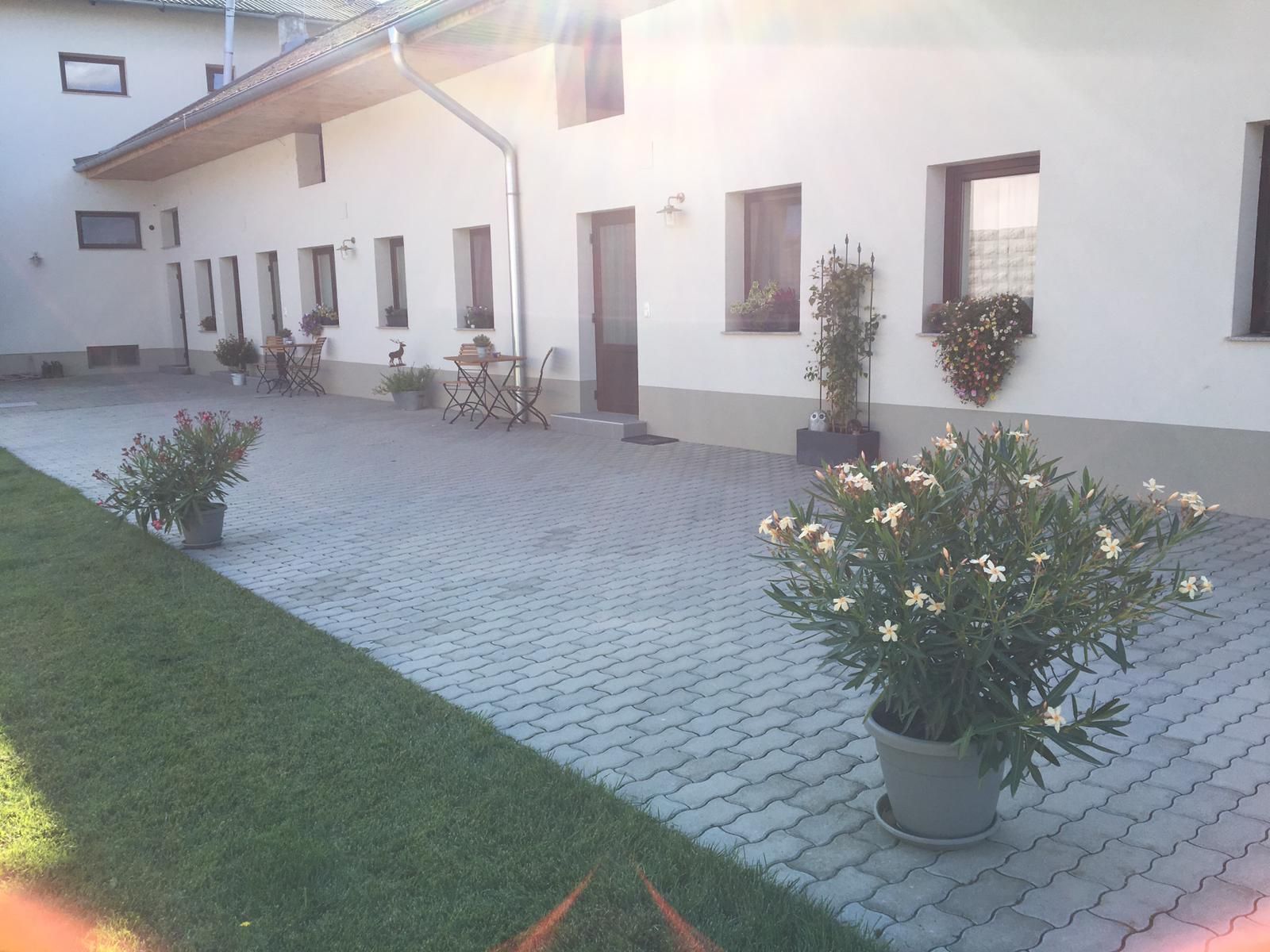 Gepflasterter Hof mit Topfpflanzen und Sitzgelegenheiten vor einem weißen Gebäude.