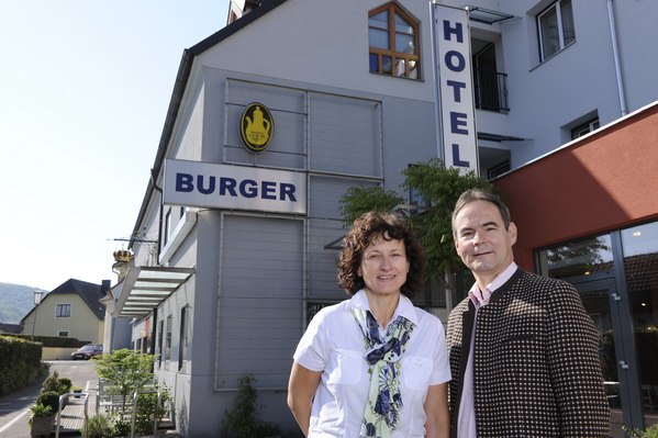 Ein Mann und eine Frau stehen vor einem Gebäude mit der Aufschrift 'Hotel Burger'.