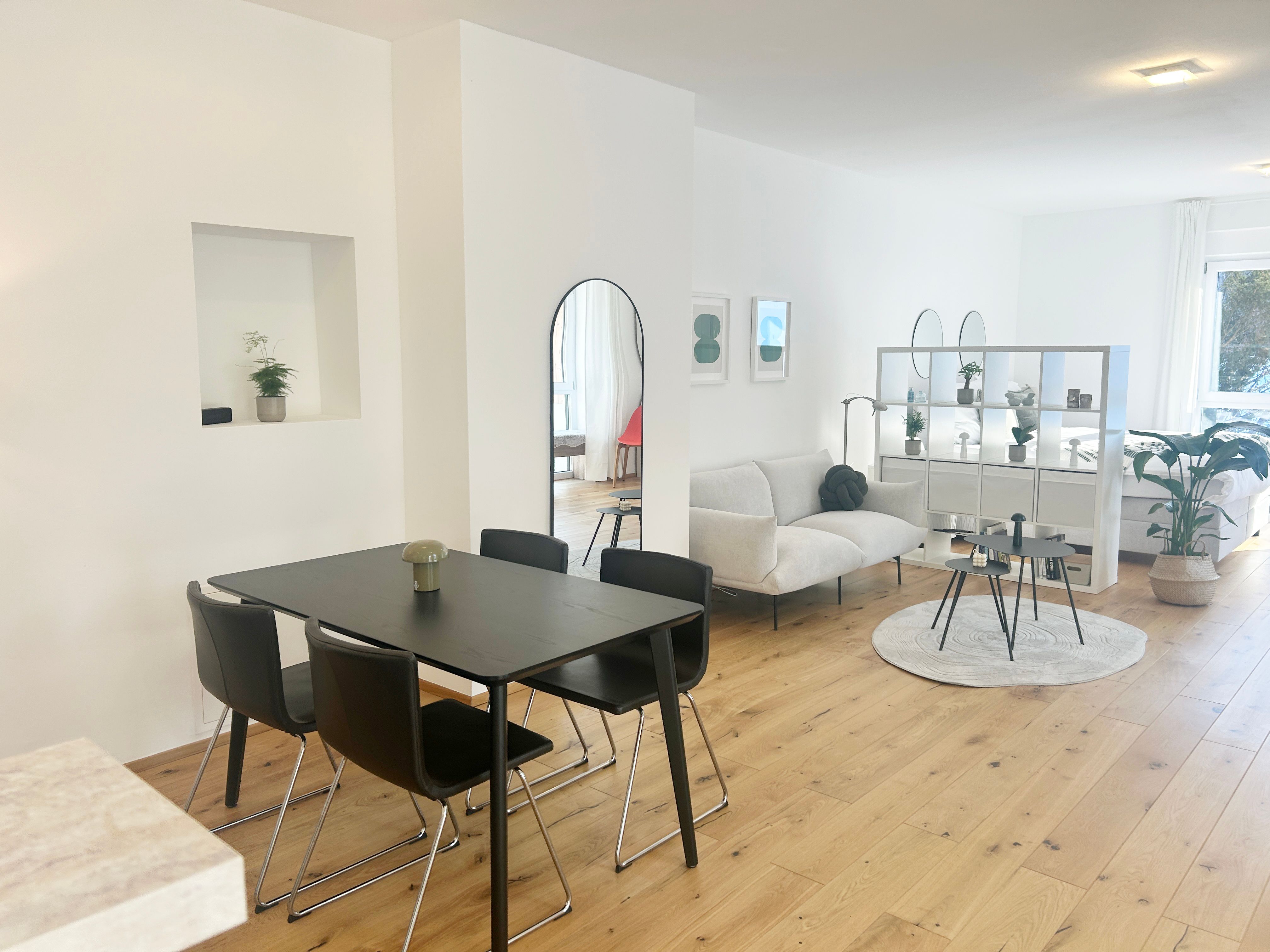Modernes Wohnzimmer mit Esstisch, Sofa und Regalen in einem offenen Raum.