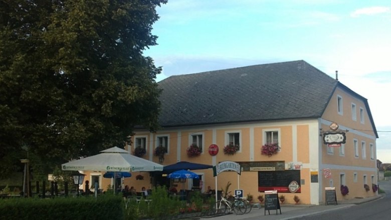Vorderansicht eines traditionellen Gasthauses mit Biergarten und Sonnenschirmen.