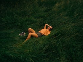 Eine Frau liegt inmitten auf einer Wiese, umgeben von hohem Gras und macht eine Pause