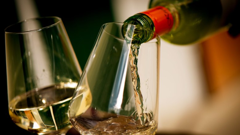 Weißwein wird in ein Glas eingeschenkt, daneben ein weiteres gefülltes Glas.