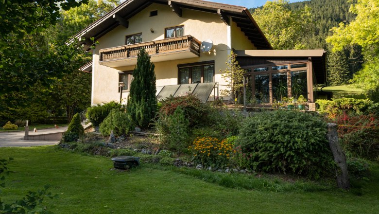 Ein zweistöckiges Ferienhaus mit Balkon und Garten, umgeben von Bäumen und Wiese.