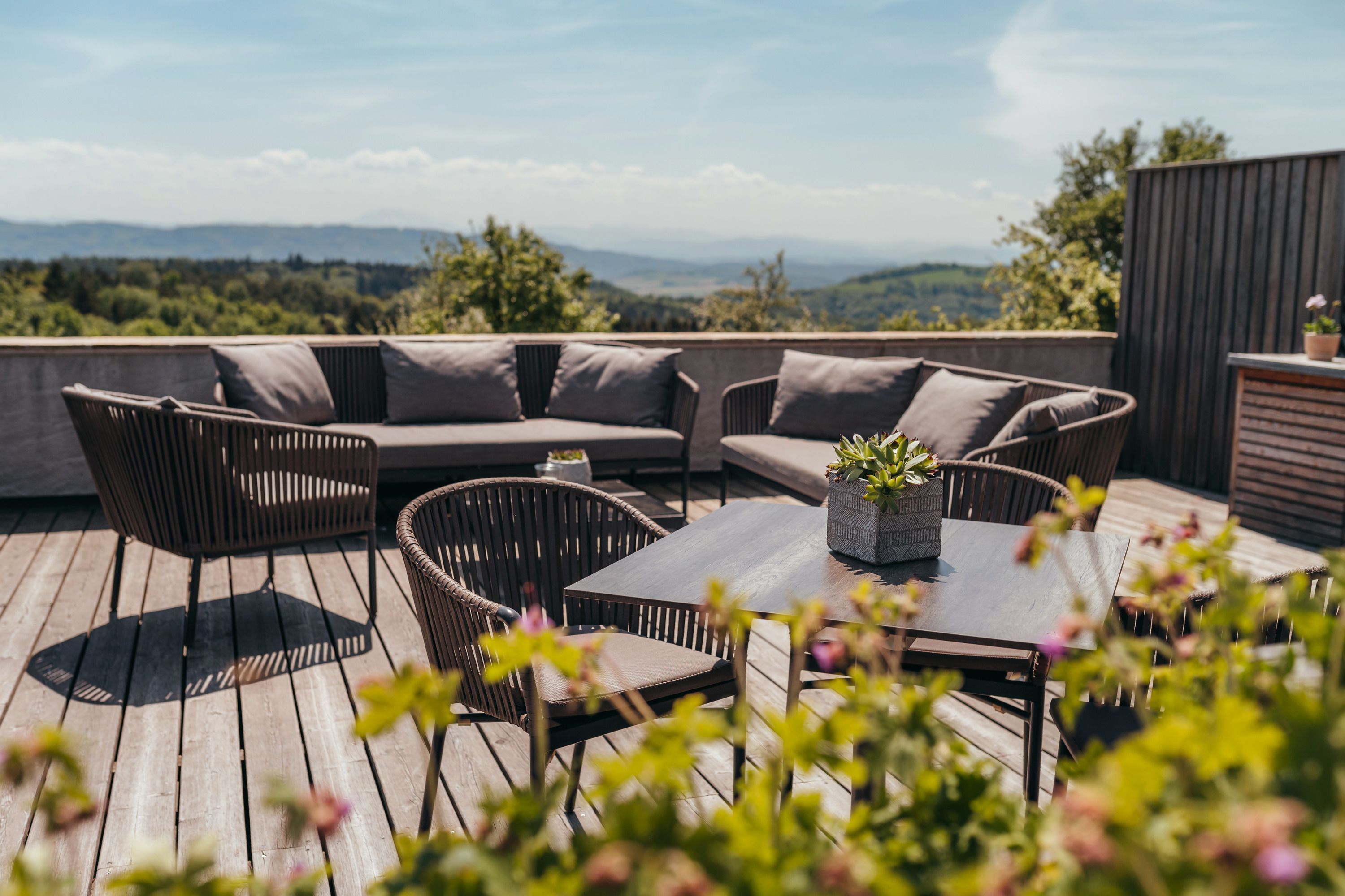 Terrasse mit Sitzmöbeln und Pflanzen, im Hintergrund eine weite Landschaft.
