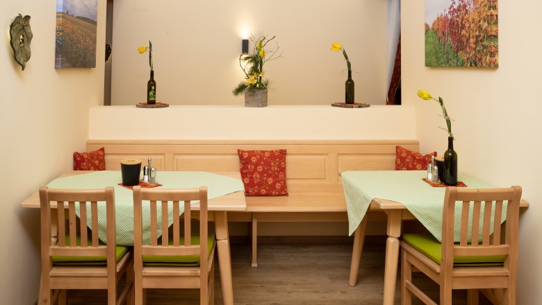 Ein gem&uuml;tlicher Fr&uuml;hst&uuml;cksraum mit Holzm&ouml;beln, gr&uuml;nen Tischdecken und gelben Blumen in Flaschenvasen. An den W&auml;nden h&auml;ngen Landschaftsbilder.