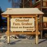 Holzschild mit der Aufschrift 'Ofnerhof Fam. Gruber Urlaub am Bauernhof' im Schnee.