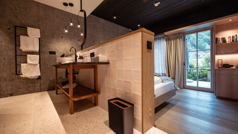 Modernes Hotelzimmer mit offenem Badezimmer, Holzboden und gro&szlig;en Fenstern mit Blick ins Gr&uuml;ne.