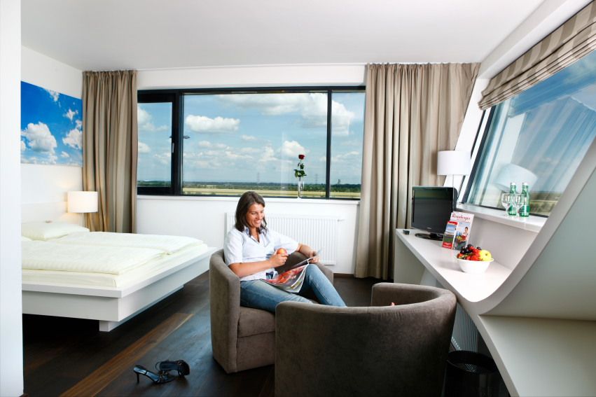 Frau sitzt in einem modernen Hotelzimmer mit großem Fenster und liest eine Zeitschrift.
