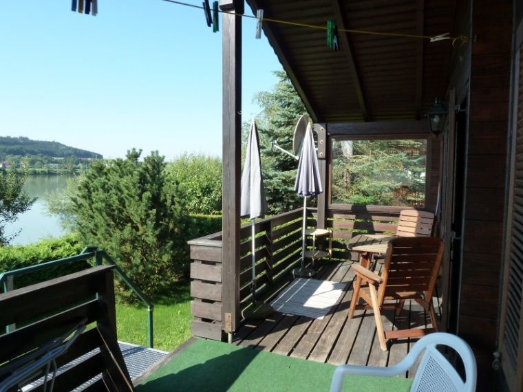 Holzterrasse eines Ferienhauses mit Blick auf einen See und grüne Landschaft.
