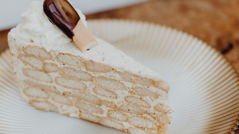 Ein Stück Malakofftorte auf einem Teller, dekoriert mit Sahne und einem Schokoladenkeks.