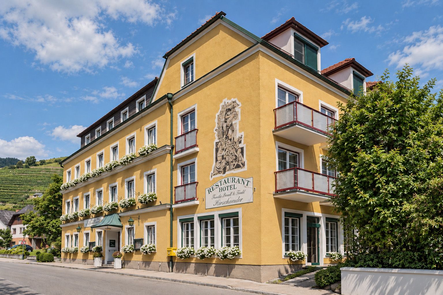 Außenansicht des Weinhotels Wachau mit gelber Fassade, Balkonen, Blumen und Restaurant-Schild in der Wachau.