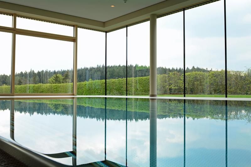 Innenpool mit großen Fenstern und Blick auf Wald und Hecken.