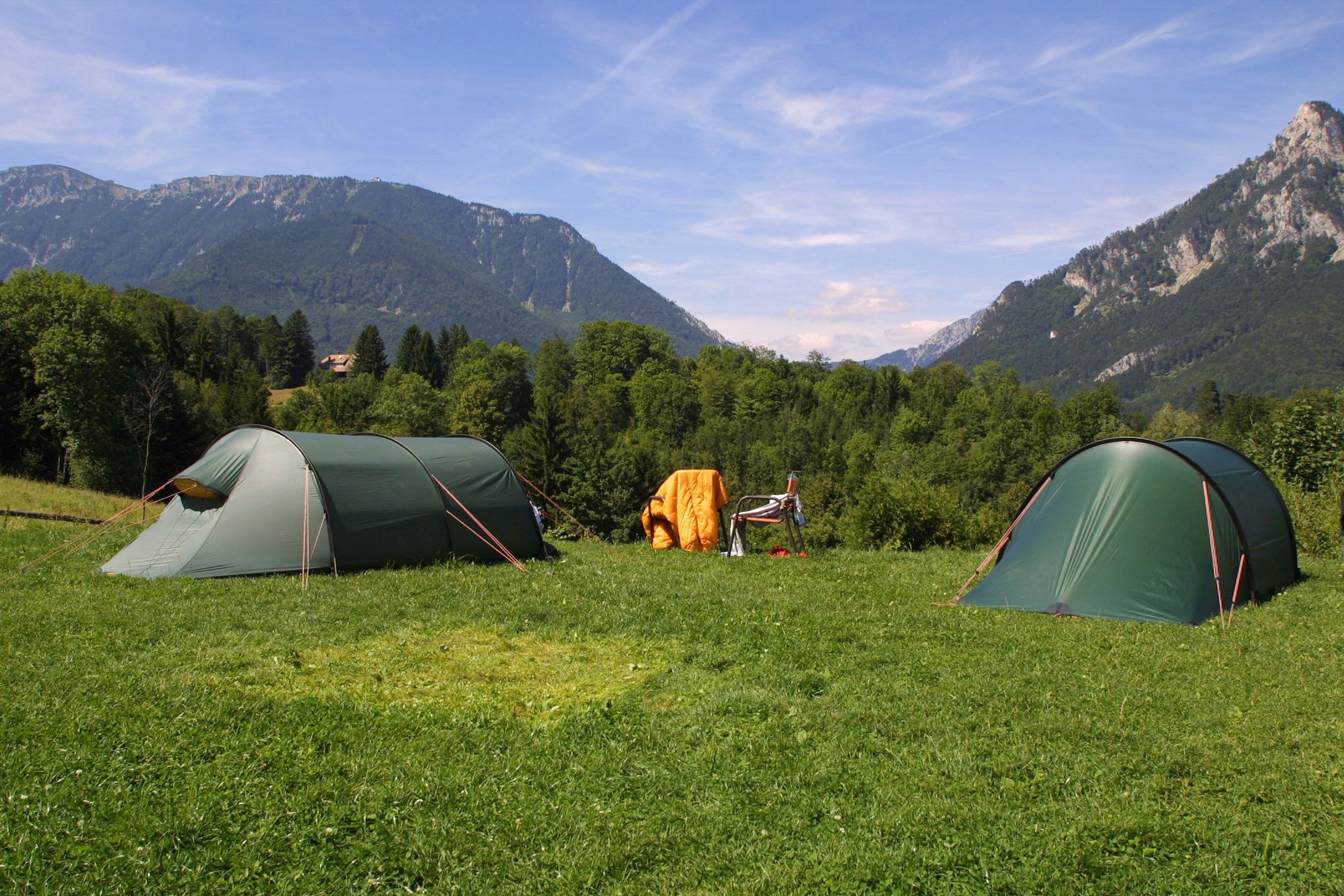Zwei grüne Zelte auf einer Wiese mit Bergen im Hintergrund.