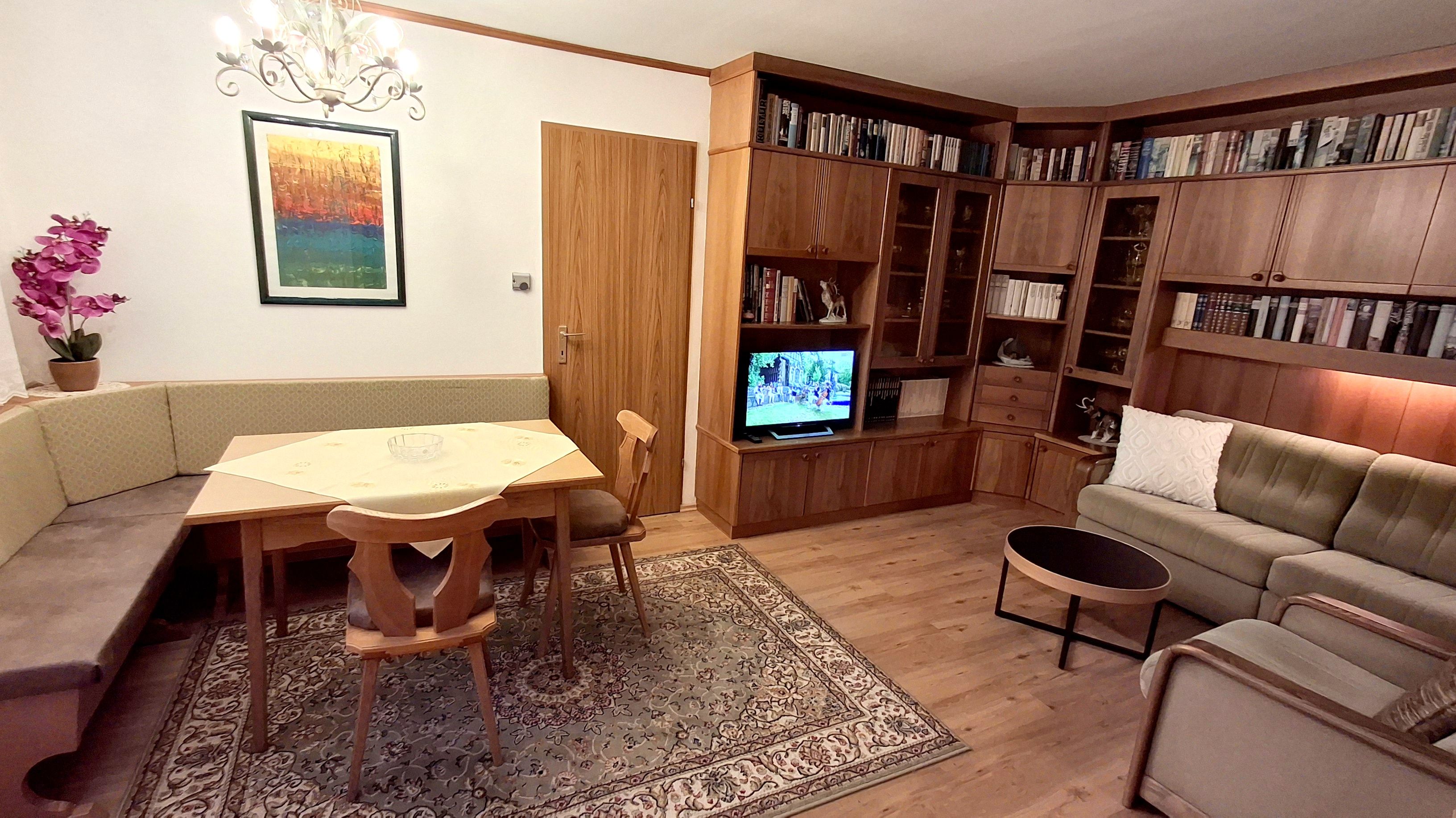 Gemütlicher Wohnbereich mit Eckbank, Holzmöbeln, Teppich und Fernseher.