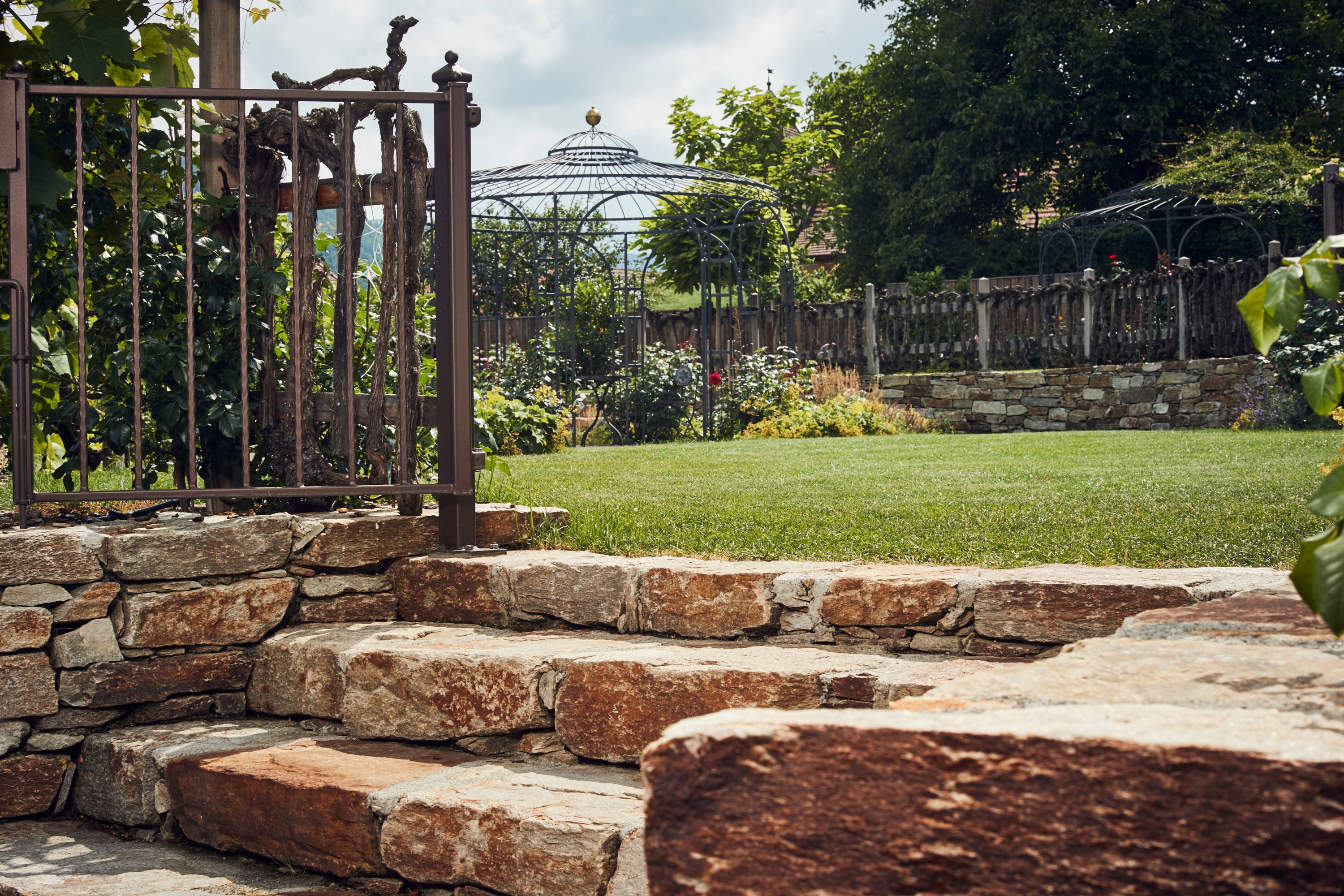 Steintreppe im Garten mit Metallzaun und Pavillon im Hintergrund.