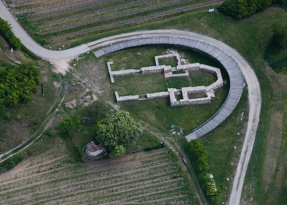 Luftaufnahme einer archäologischen Ausgrabungsstätte mit einem halbkreisförmigen Steg.