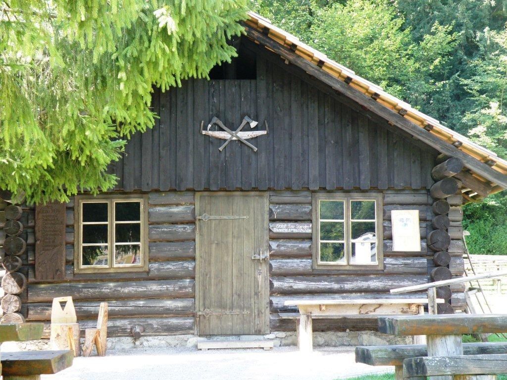 Holzhütte mit zwei Fenstern und einer Tür, umgeben von Bäumen.