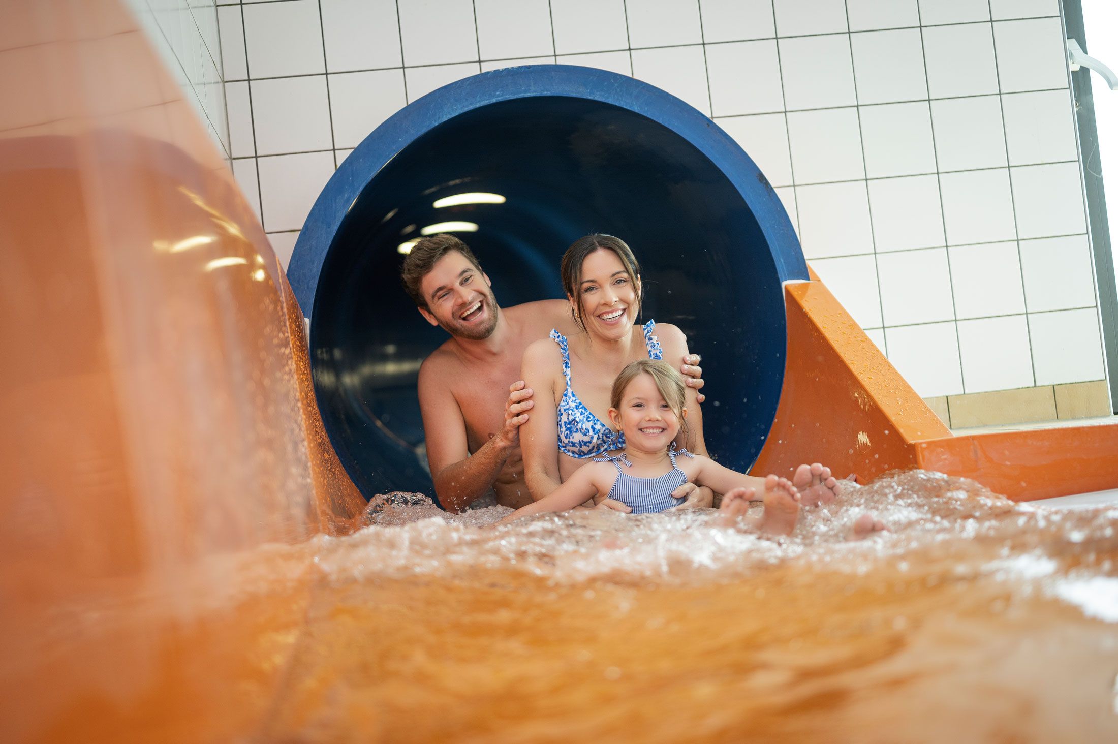 Eine Familie rutscht lachend eine Wasserrutsche hinunter.