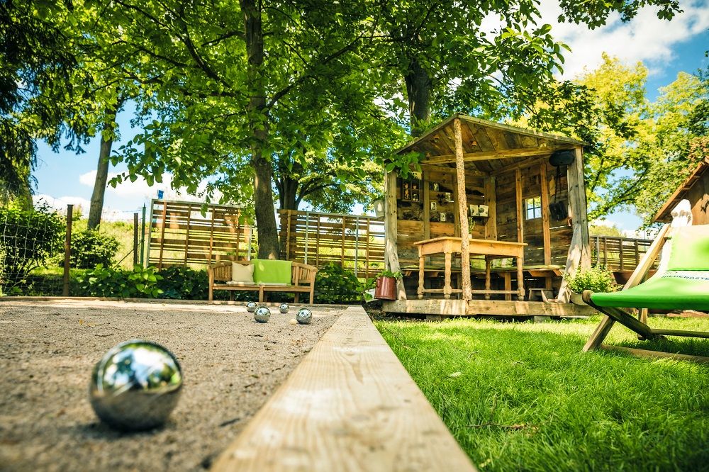 Garten mit Laube und Sandfläche mit Boccia Kugel, daneben Liegestuhl