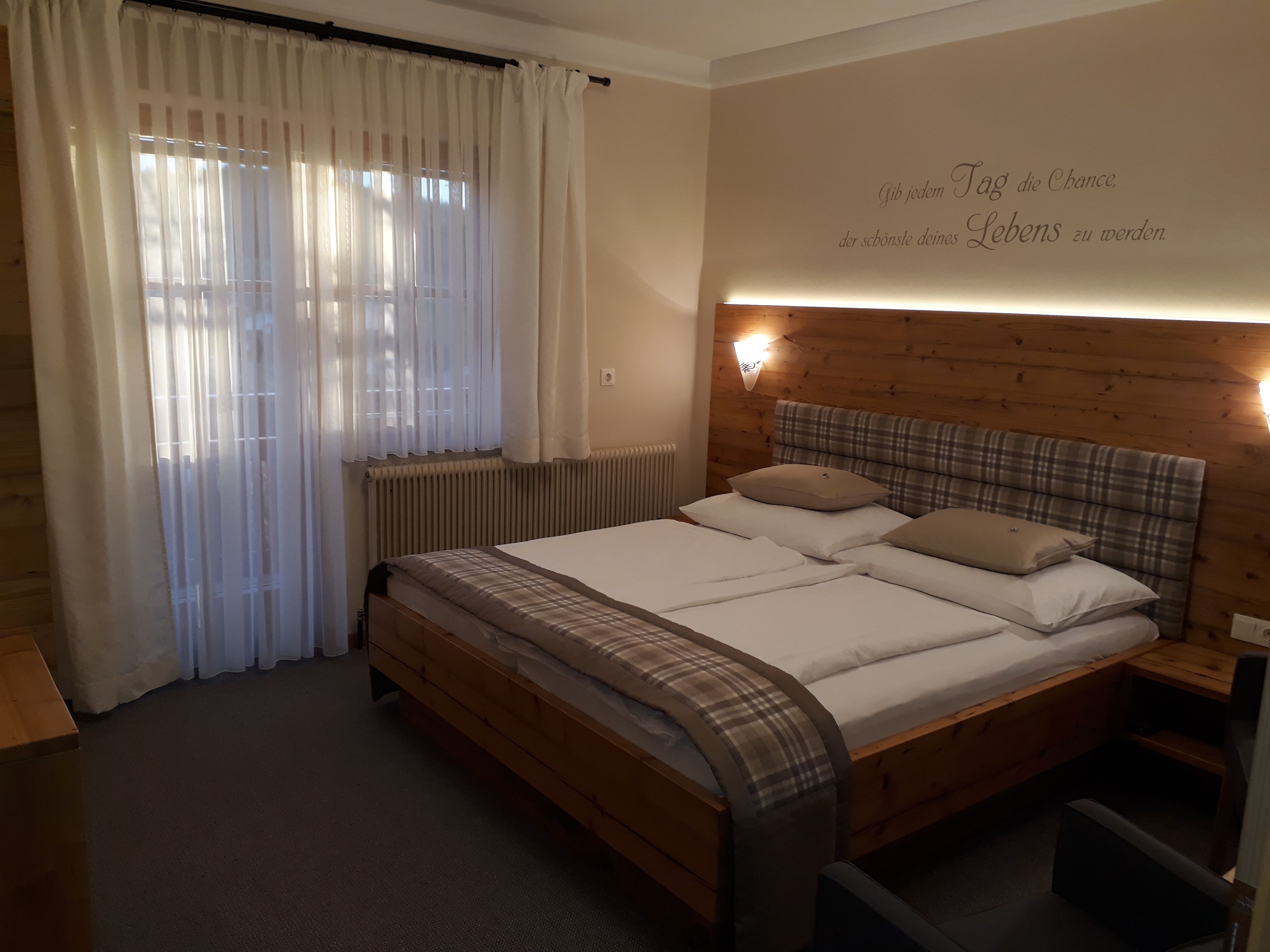 Gemütliches Schlafzimmer mit Doppelbett, Holzwand und Vorhängen.