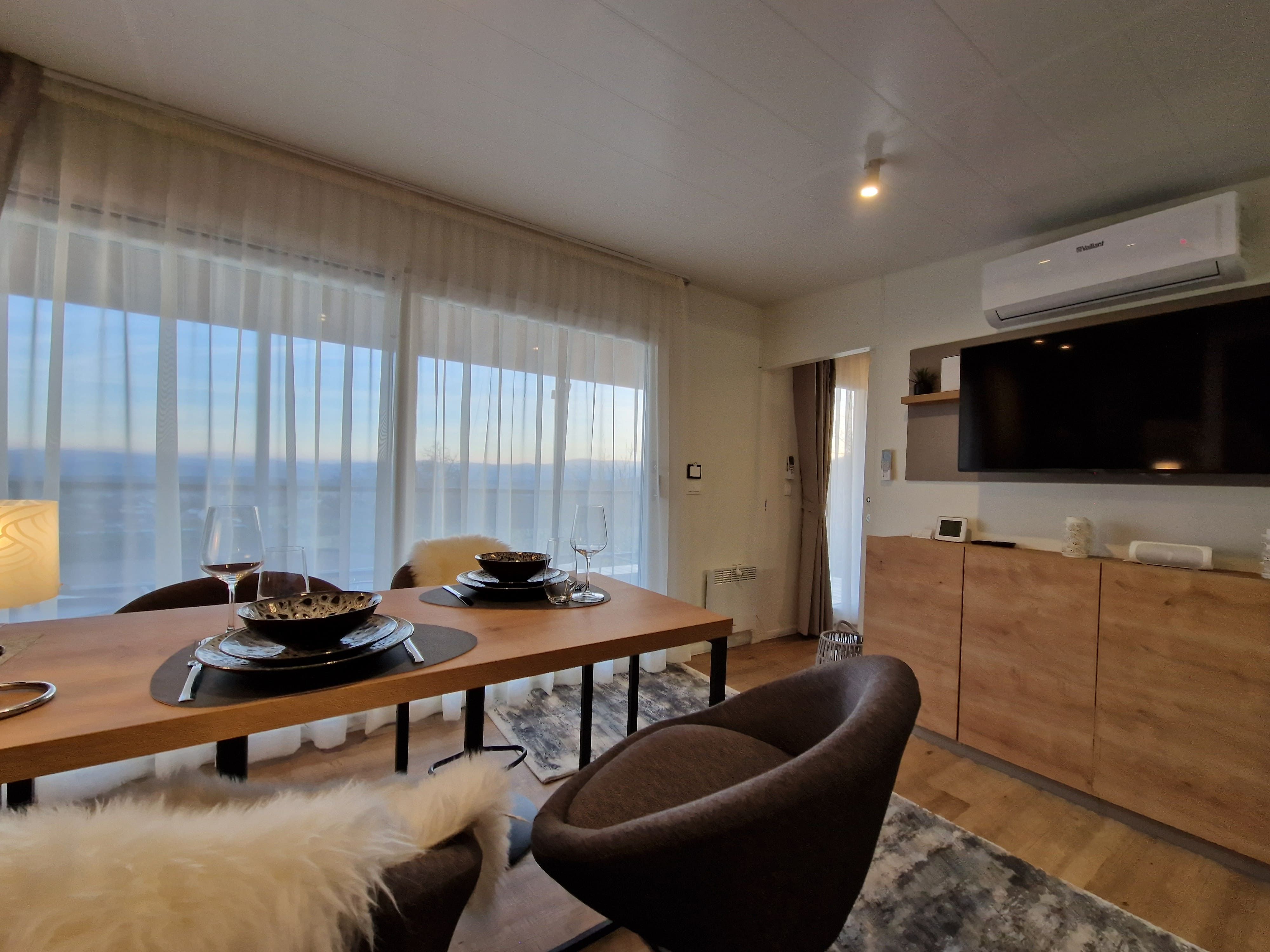 Modernes Wohnzimmer mit Esstisch, Stühlen, großem Fenster und Fernseher.