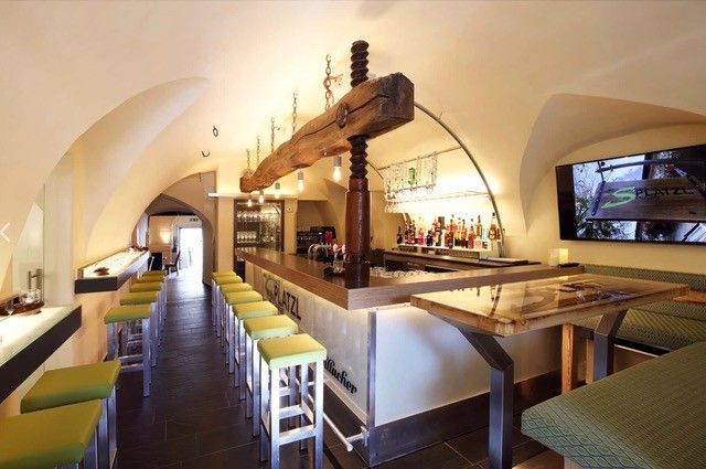 Innenansicht eines modernen Restaurants mit Bar, grünen Hockern und gewölbter Decke.