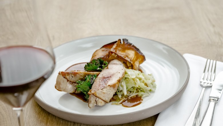 Ein Teller mit Fasanbrust, Grünkohl und Kraut, daneben ein Glas Rotwein.