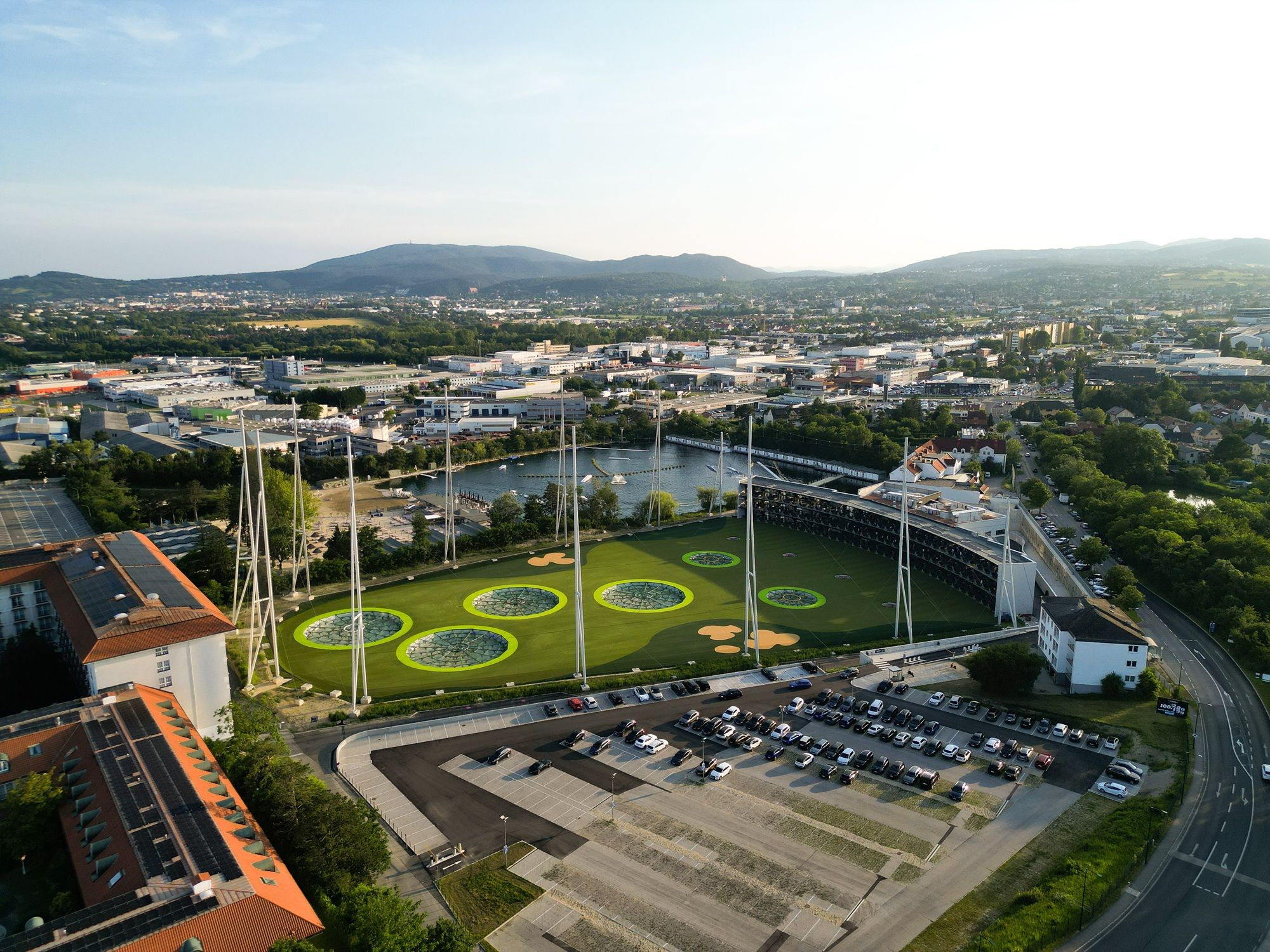 Außenansicht der Anlage Top Golf, Nebengebäude, Parkplatz und Netze rund um die Anlage.