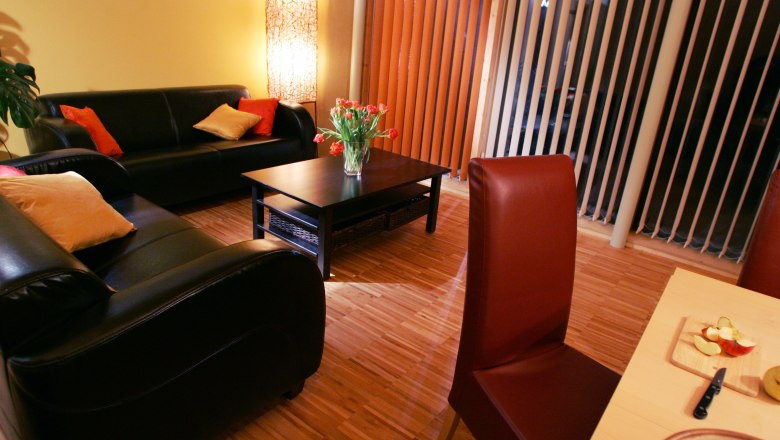 Gem&uuml;tliches Wohnzimmer mit Ledersofas, Couchtisch, Blumenstrau&szlig; und Esstisch mit Obst.