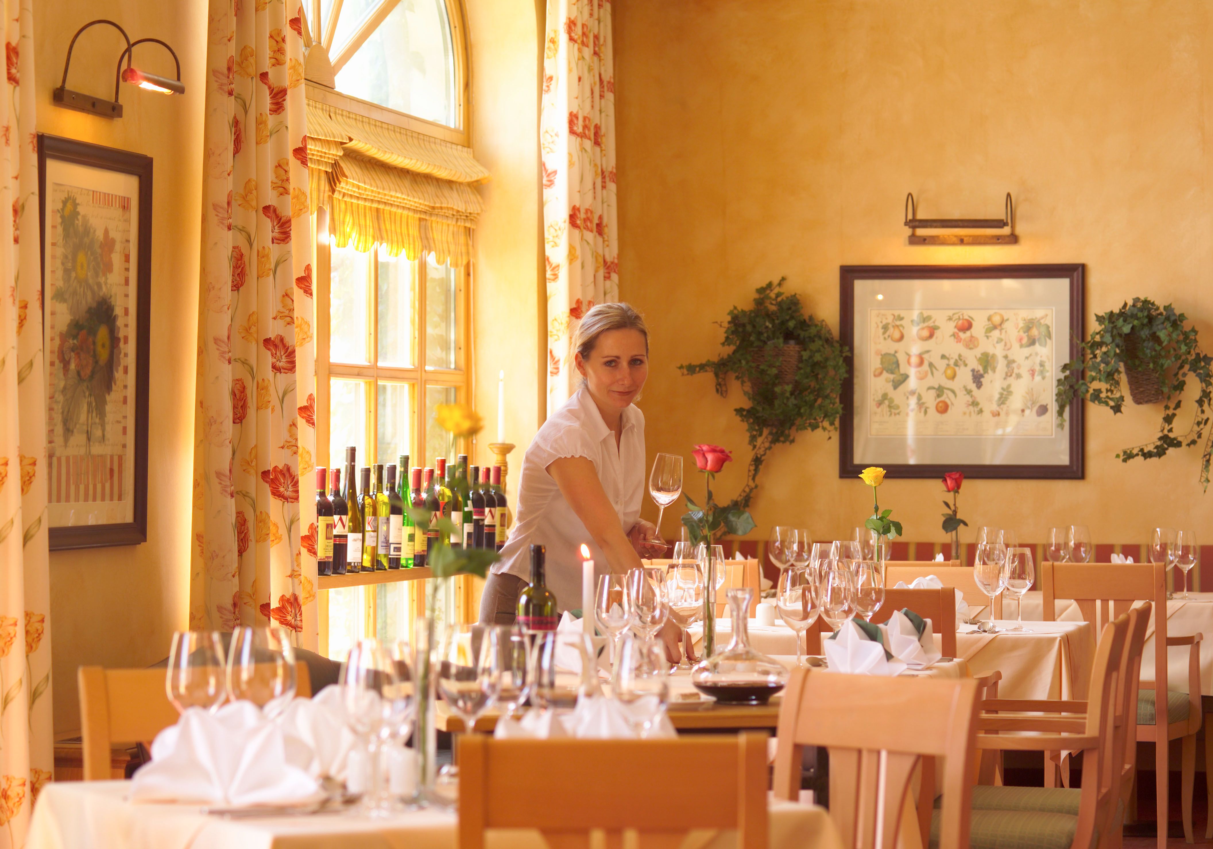 Eine Frau deckt Tische in einem eleganten Restaurant mit Weingläsern und Blumen.