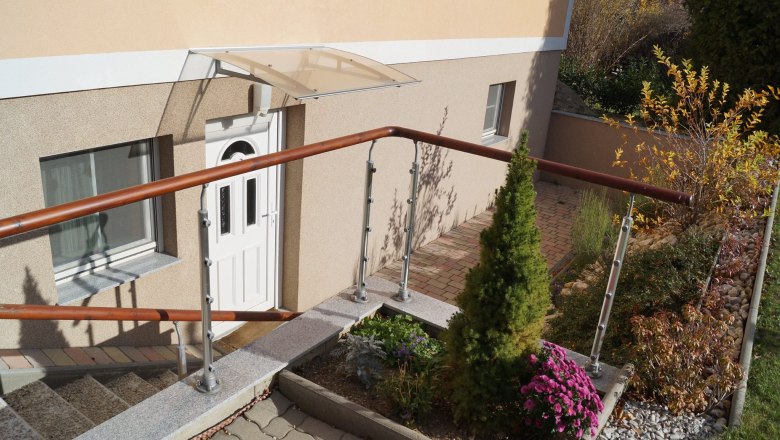 Eingangsbereich eines Hauses mit wei&szlig;er T&uuml;r, Gel&auml;nder und Garten.