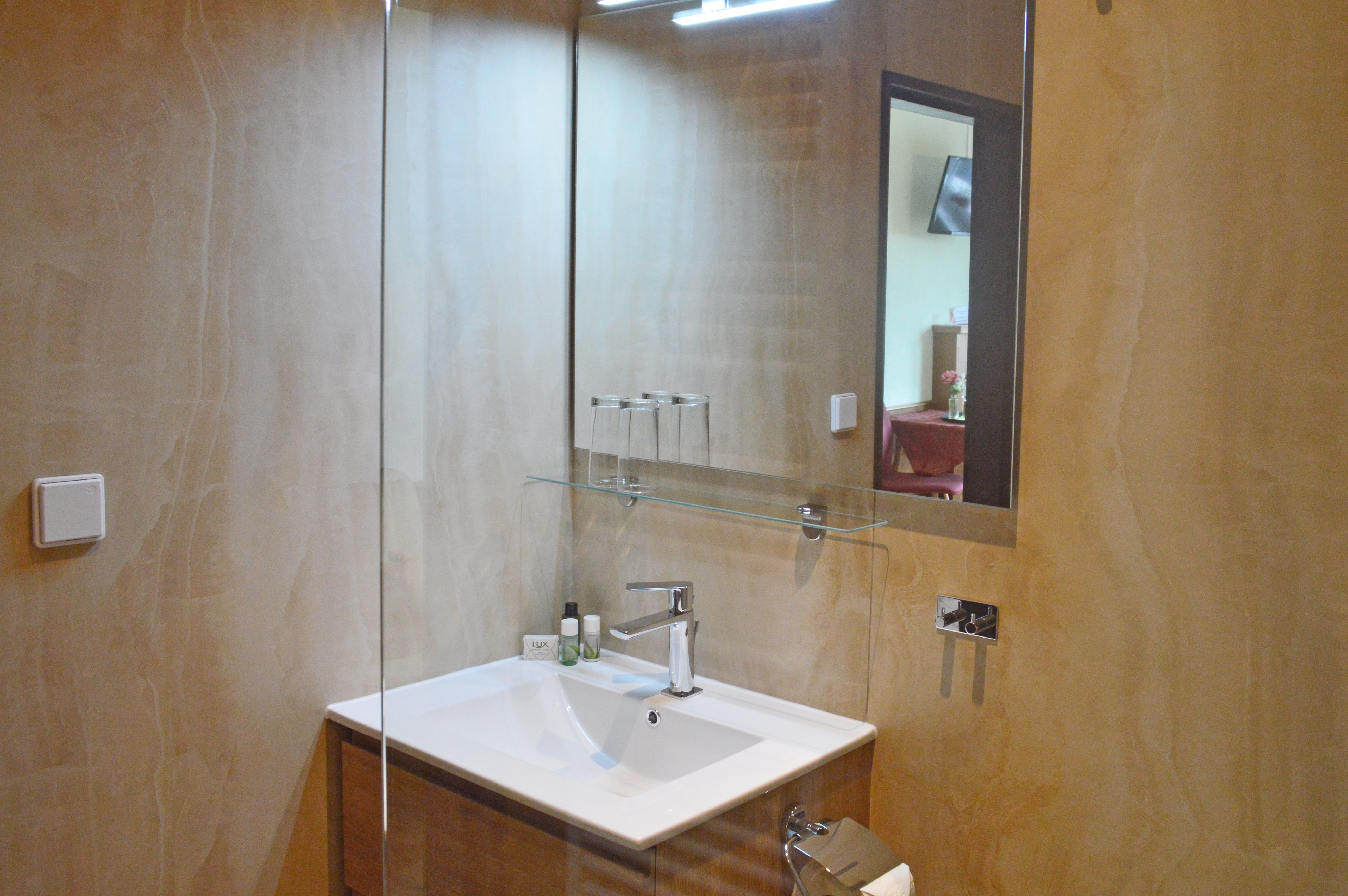 Modernes Badezimmer mit Waschbecken, Spiegel und Glasregal.