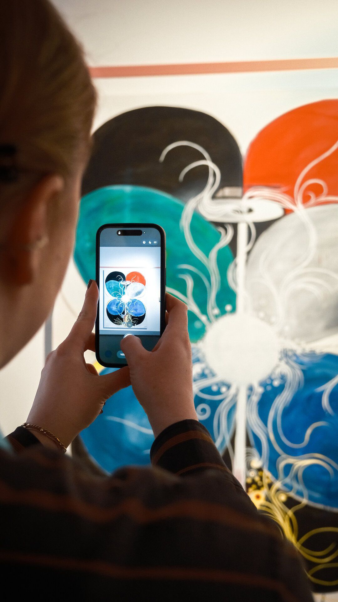 Besucherin fotografiert ein abstraktes, farbiges Kunstwerk in der Niederösterreichischen Landesausstellung 2026 mit ihrem Smartphone.
