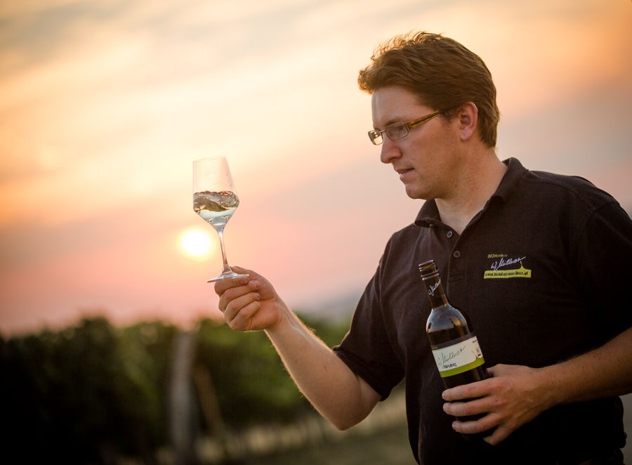 Ein Mann hält ein Weinglas und eine Weinflasche bei Sonnenuntergang im Weinberg.