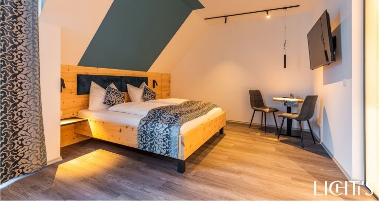Modernes Doppelzimmer mit Holzbett, zwei St&uuml;hlen und einem Tisch, Fernseher an der Wand.