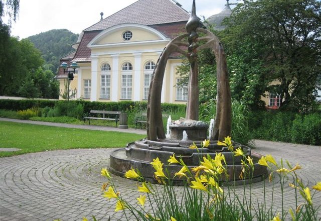 Brunnen vor einem historischen Geb&auml;ude mit gelben Blumen im Vordergrund.