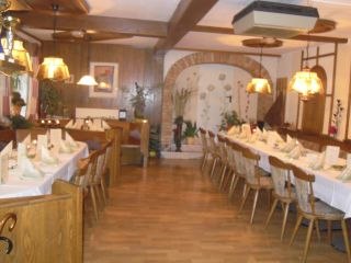 Ein gem&uuml;tlicher Speiseraum mit langen, gedeckten Tischen und Holzst&uuml;hlen, dekoriert mit Lampen und Pflanzen.