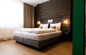 Modernes Hotelzimmer mit großem Bett, Holzwand und hängenden Lampen.