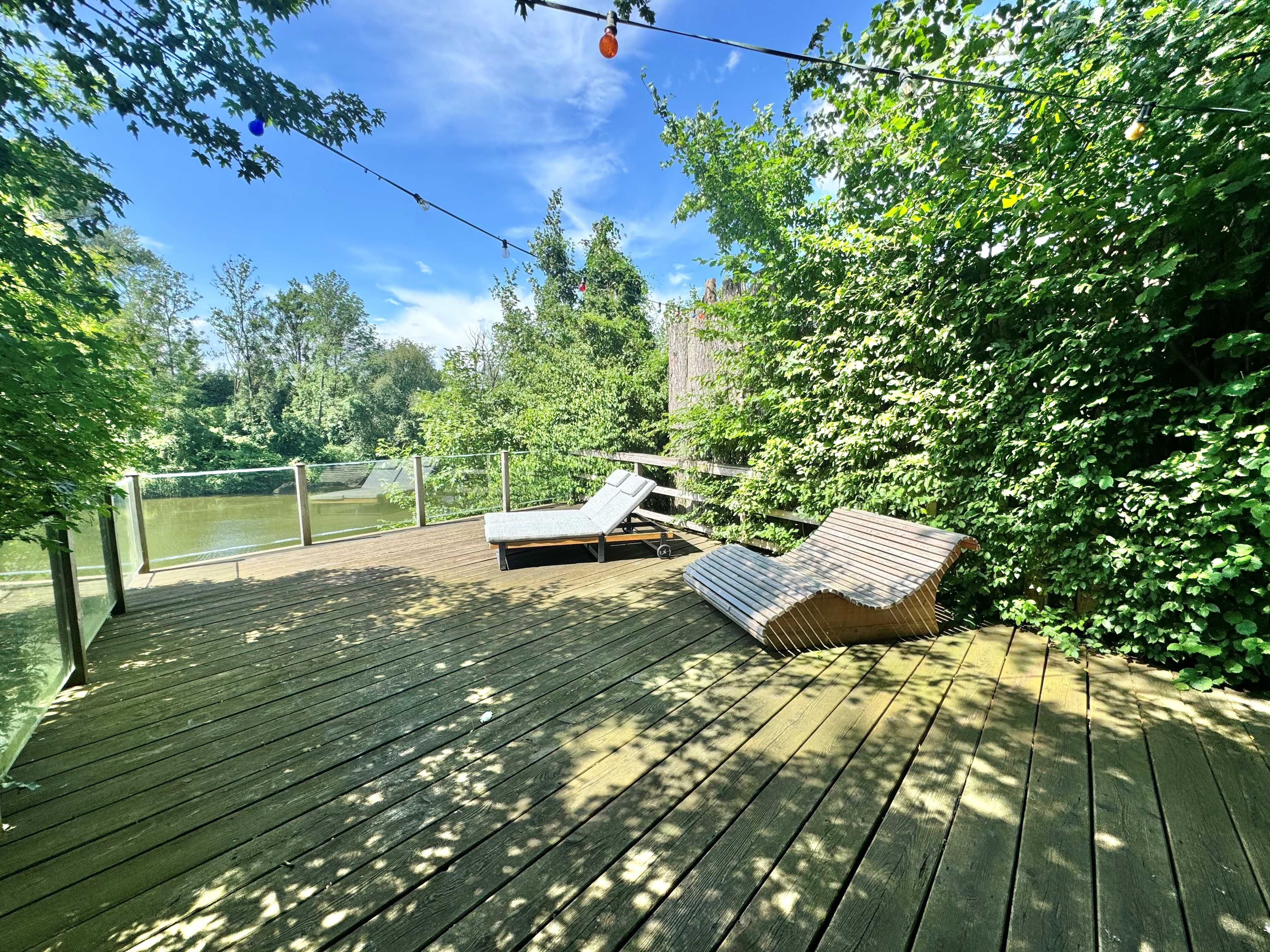 Holzterrasse mit Liegestühlen und Blick auf den Fluss Ybbs, umgeben von Bäumen.