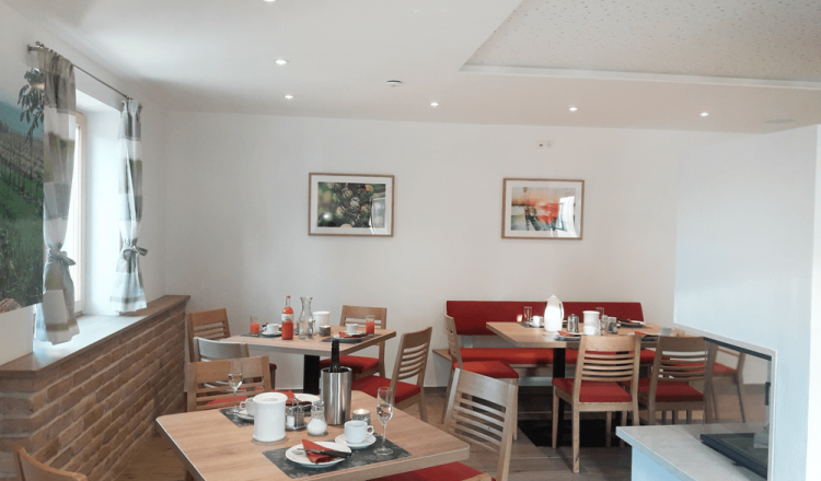 Ein gemütlicher Frühstücksraum mit Holztischen, roten Polsterbänken und dekorativen Bildern an der Wand.