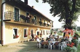 Ein Gasthof mit Terrasse, auf der Menschen an Tischen sitzen, umgeben von Sonnenschirmen und Blumen.