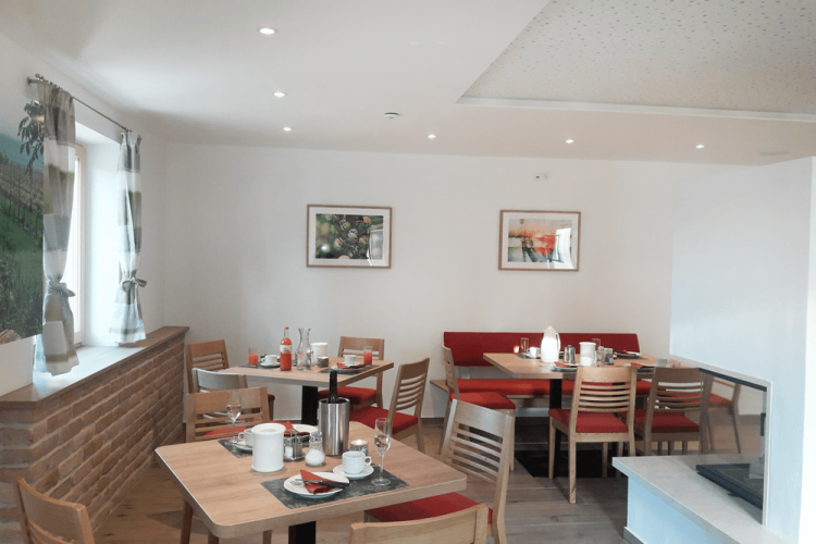 Ein gemütlicher Frühstücksraum mit Holztischen, roten Polsterbänken und dekorativen Bildern an der Wand.