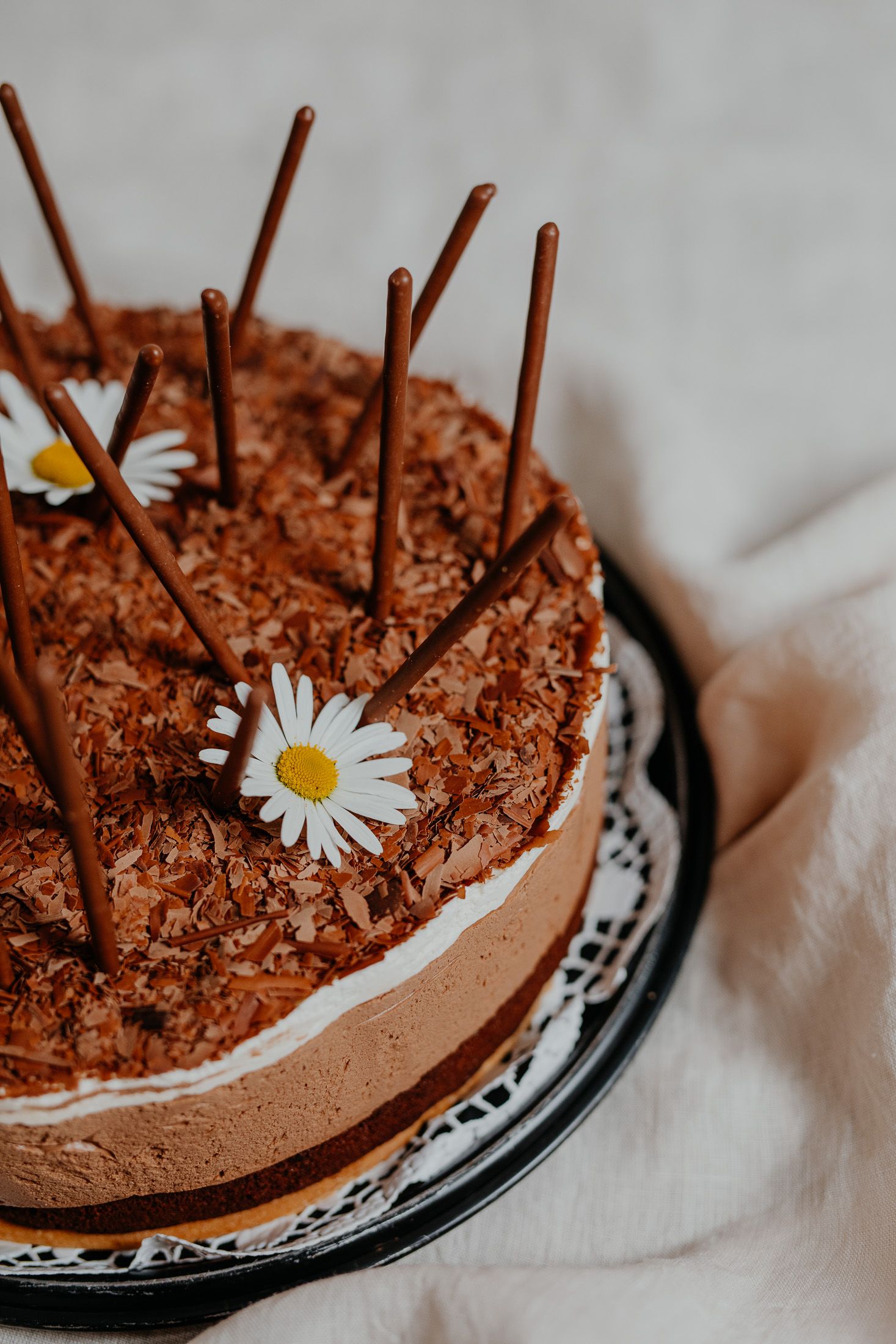 Schokoladentorte mit Schokostäbchen und Gänseblümchen dekoriert.