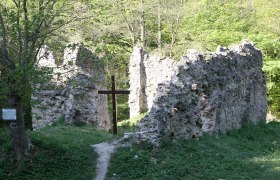 Ruinen eines alten Klosters mit einem Holzkreuz im Vordergrund, umgeben von B&auml;umen.