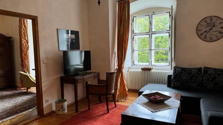 Gem&uuml;tliches G&auml;stezimmer mit Sofa, Tisch, Fernseher und gro&szlig;em Fenster.