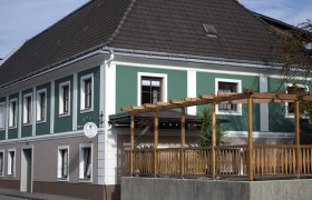 Außenansicht einer Frühstückspension mit grün-weißer Fassade und Holzpergola.